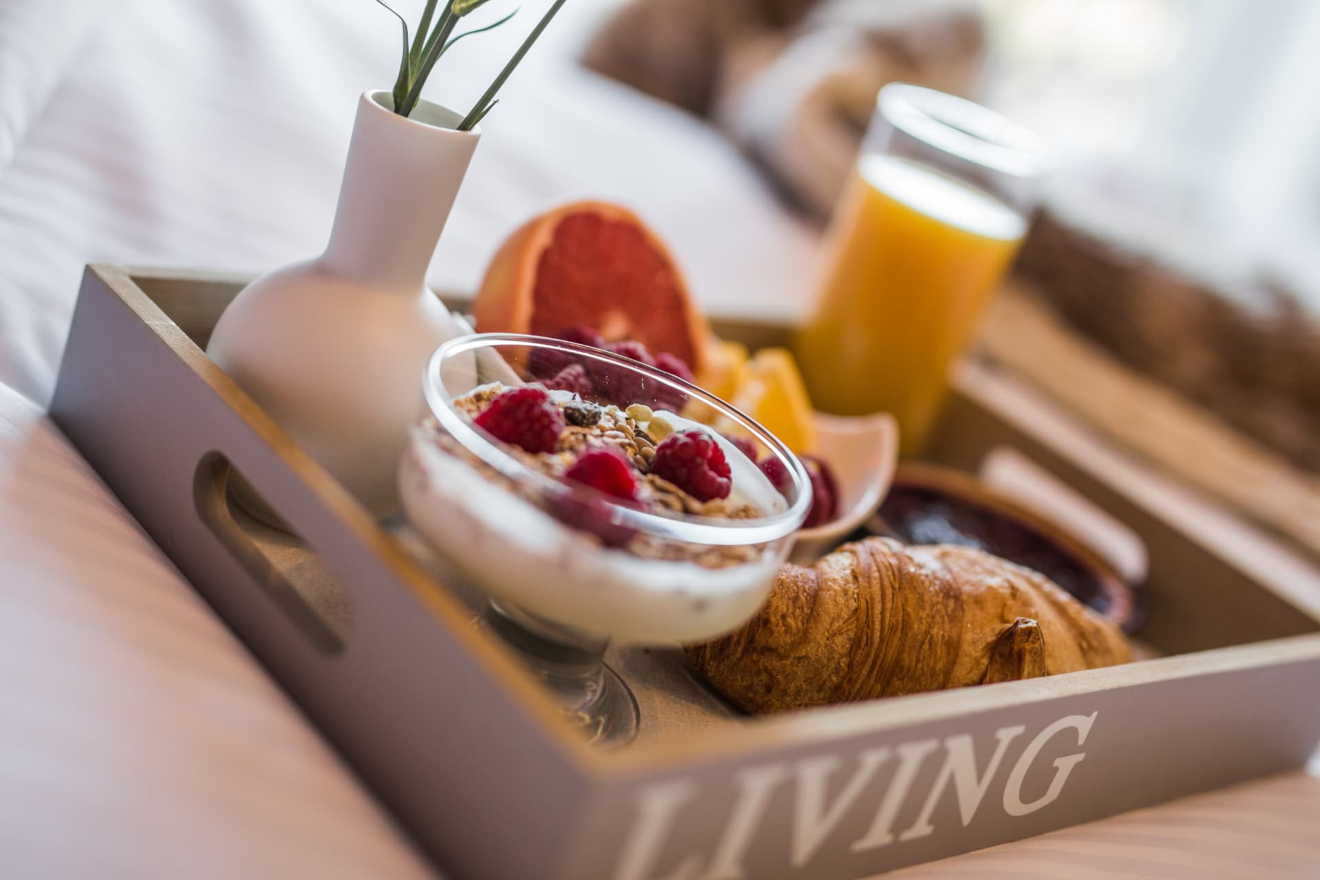 Taca śniadaniowa na łóżku: jogurt z malinami, croissant, sok i owoce